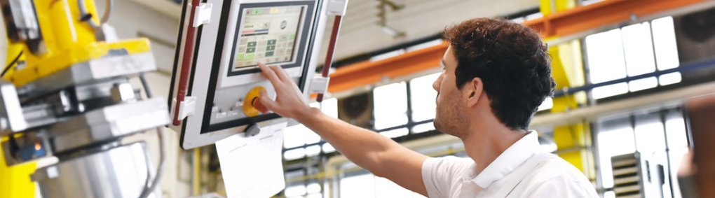 Umschulung Maschinen- und Anlagenführer Mann in Werkstatt blick auf einen CNC-Monitor hoch und nimmt Einstellungen vor.