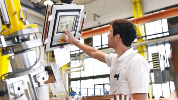 Mann in Werkstatt blick auf einen CNC-Monitor hoch und nimmt Einstellungen vor.