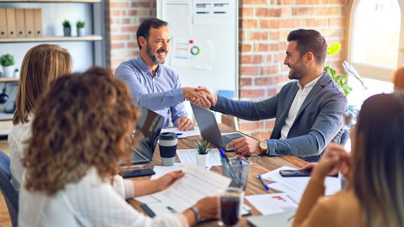 Eine Gruppe von Geschäftsleuten, die glücklich und selbstbewusst lächeln. Sie arbeiten zusammen, lächeln dabei und schütteln sich im Büro die Hände.