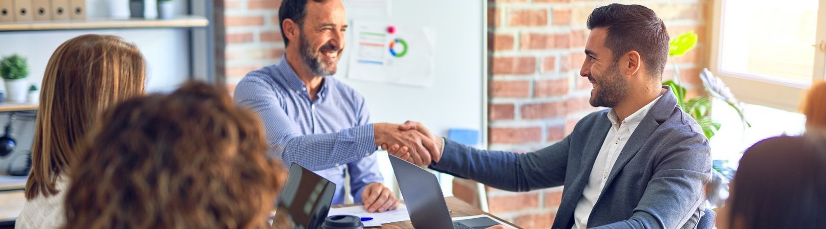 Grundlagen Personalwesen, Personalbeschaffung und Entgeltabrechnung Eine Gruppe von Geschäftsleuten, die glücklich und selbstbewusst lächeln. Sie arbeiten zusammen, lächeln dabei und schütteln sich im Büro die Hände.