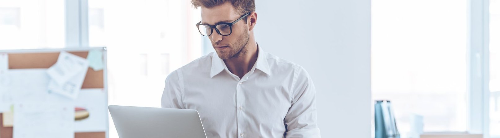 Personalreferent mit Betrieblichem Eingliederungsmanagement (BEM) Gepflegter junger Mann mit Brille, der seinen Laptop benutzt, während er sich am Tisch im Büro lehnt.