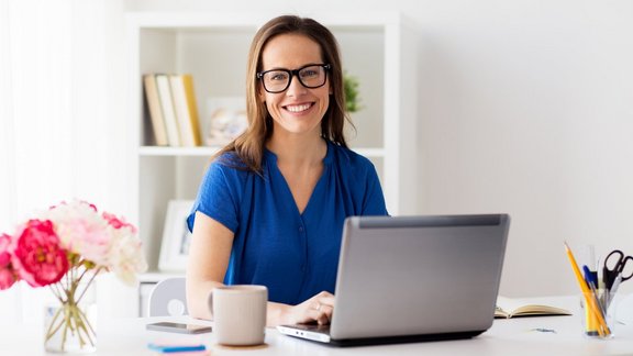 Glückliche Frau arbeitet mit einem Laptop zu Hause oder im Büro – Teilnehmerin des Kurses 'Basiswissen Wirtschaftsenglisch', um Englischkenntnisse am Arbeitsplatz zu verbessern.