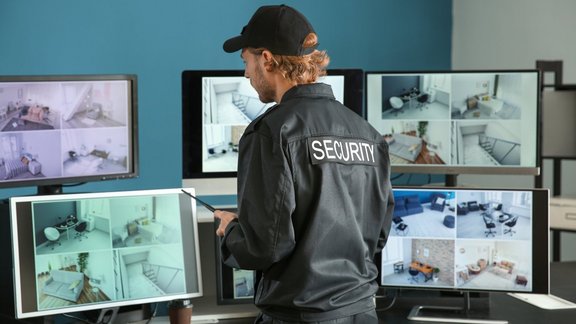 Ein Sicherheitsbeamter schaut auf 7 Monitore in einem Überwachungsraum.