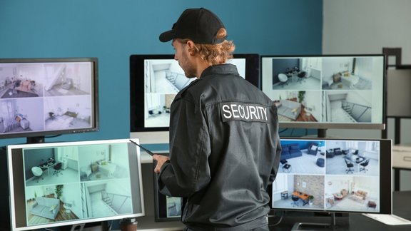 Ein Sicherheitsbeamter schaut auf 7 Monitore in einem Überwachungsraum.