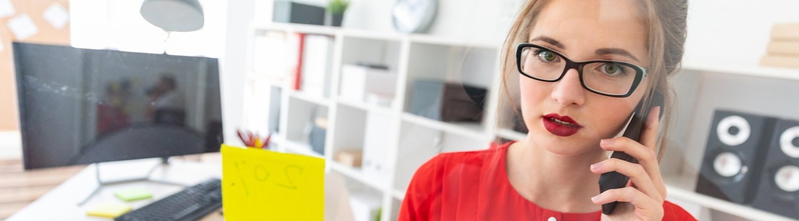 Umschulung Industriekaufleute Junge Frau mit Brille und rotem Shirt arbeitet im Büro mit Post-its. Foto mit Tiefenschärfe.