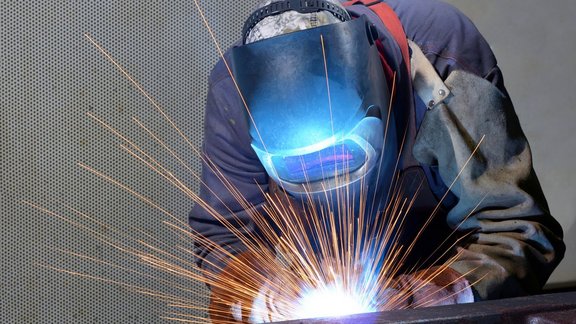 Teilnehmender der Fortbildung Schweißtechnik beim Schweißen von Metallteilen. Der Teilnehmende hält eine Schweißmaske vor dem Gesicht, es fliegen Funken.