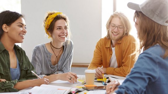 Porträt von multikulturell motivierten Studierenden, die von Büchern umgeben sind, sich angeregt unterhalten, zusammenarbeiten und sich auf ein Seminar vorbereiten.