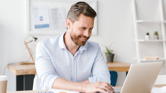 Ein lächelnder Geschäftsmann arbeitet am Laptop, während er am Schreibtisch im Büro sitzt.