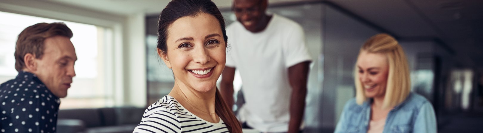 Young businesswoman looking over her shoulder and smiling while working with a group of colleagues at a table in an office