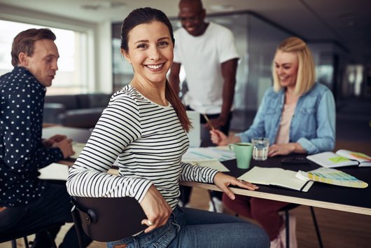 Young businesswoman looking over her shoulder and smiling while working with a group of colleagues at a table in an office